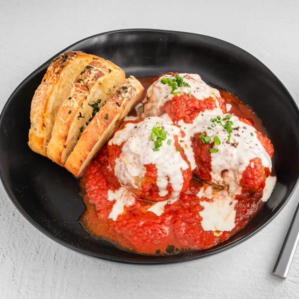 Three meatballs covered in red sauce and white cream, with a side of sliced garlic bread.