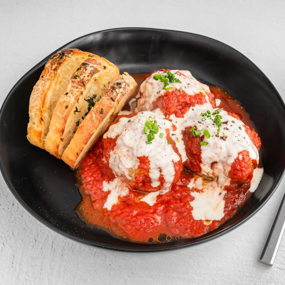 Three meatballs covered in red sauce and white cream, with a side of sliced garlic bread.