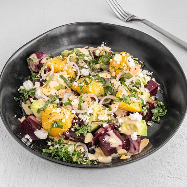 Beet and orange salad with avocado, feta, almonds, and herbs in a black bowl.