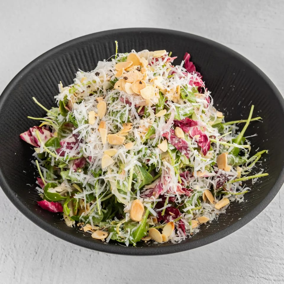 A fresh salad with mixed greens, shredded cheese, and sliced almonds in a black bowl.