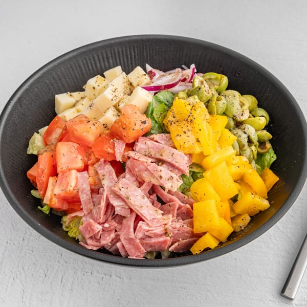 A vibrant antipasto salad in a black bowl, featuring cheese cubes, tomatoes, salami, bell peppers, and olives.