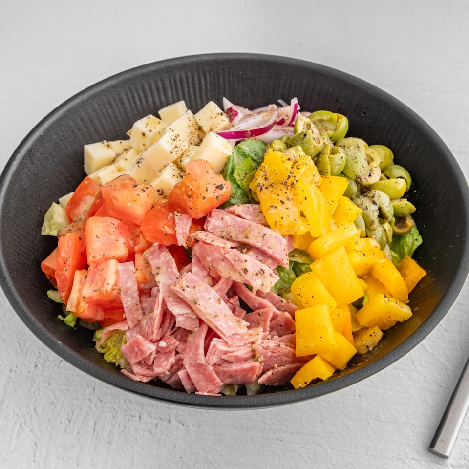 A vibrant antipasto salad in a black bowl, featuring cheese cubes, tomatoes, salami, bell peppers, and olives.