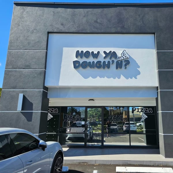 The exterior of How Ya Dough'n Pizza, a modern building with a large sign and glass entrance.
