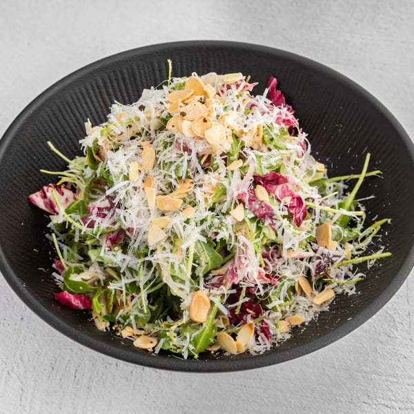 A fresh salad with mixed greens, shredded cheese, and sliced almonds in a black bowl.